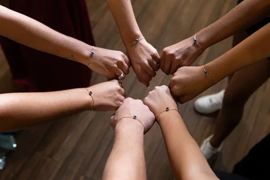 Damas com as mãos unidas em círculo, usando pulseiras