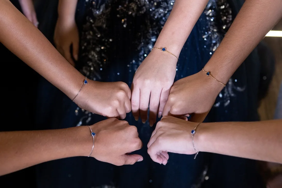 Mãos de damas unidas, com pulseiras, sobre vestido azul-marinho