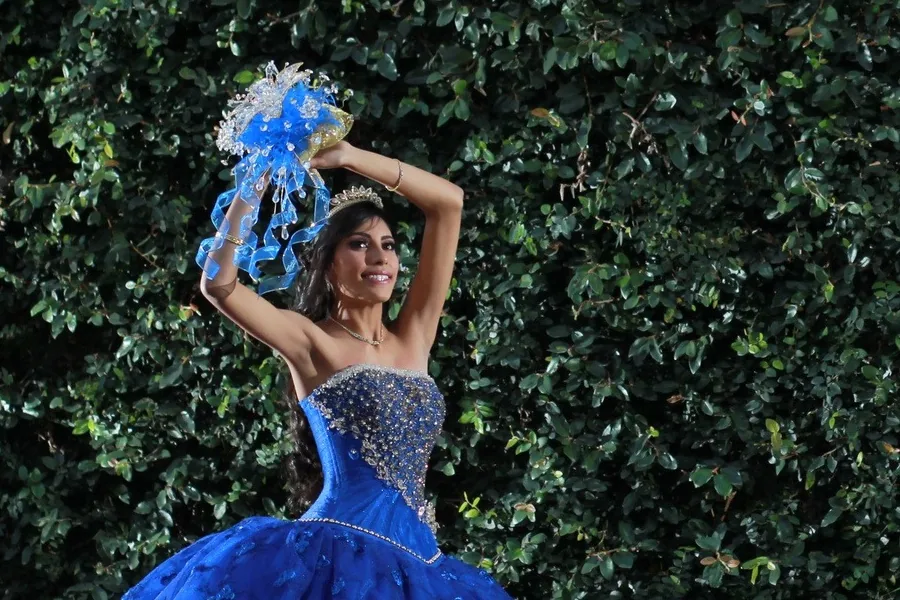 Debutante de vestido azul-royal, com tiara, colar e pulseira, segurando o buquê